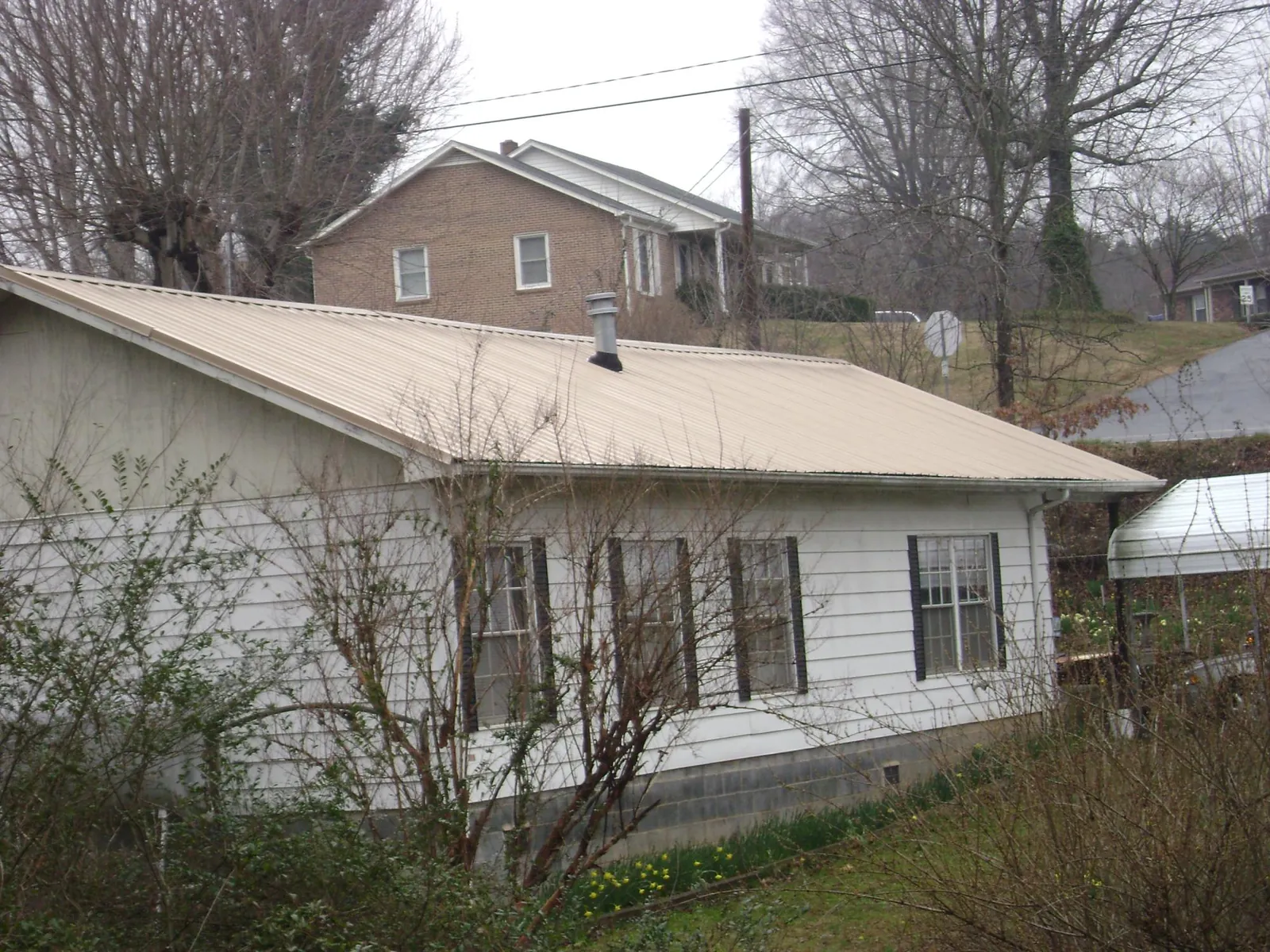 Tan metal roof on a white sided house set into a hillside — Commercial Roofing by Roofing Brothers in Adairville